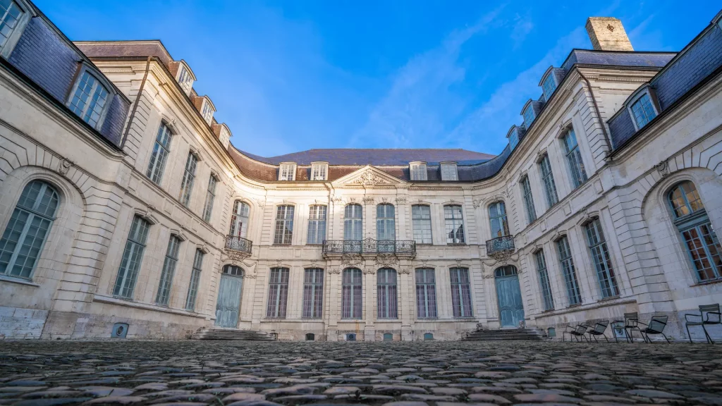 Cour pavée et façade XVIIIe du Musée Sandelin à Saint-Omer, sous un ciel bleu vif.